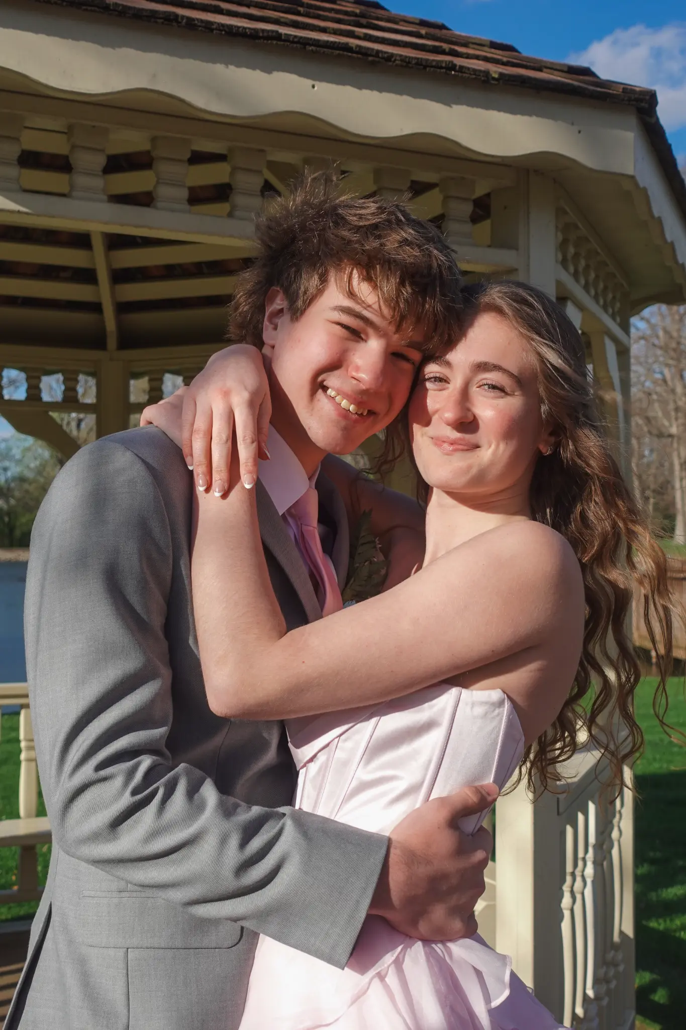 Prom couple embracing near a gazebo in bright outdoor sunlight in Northwest Indiana.