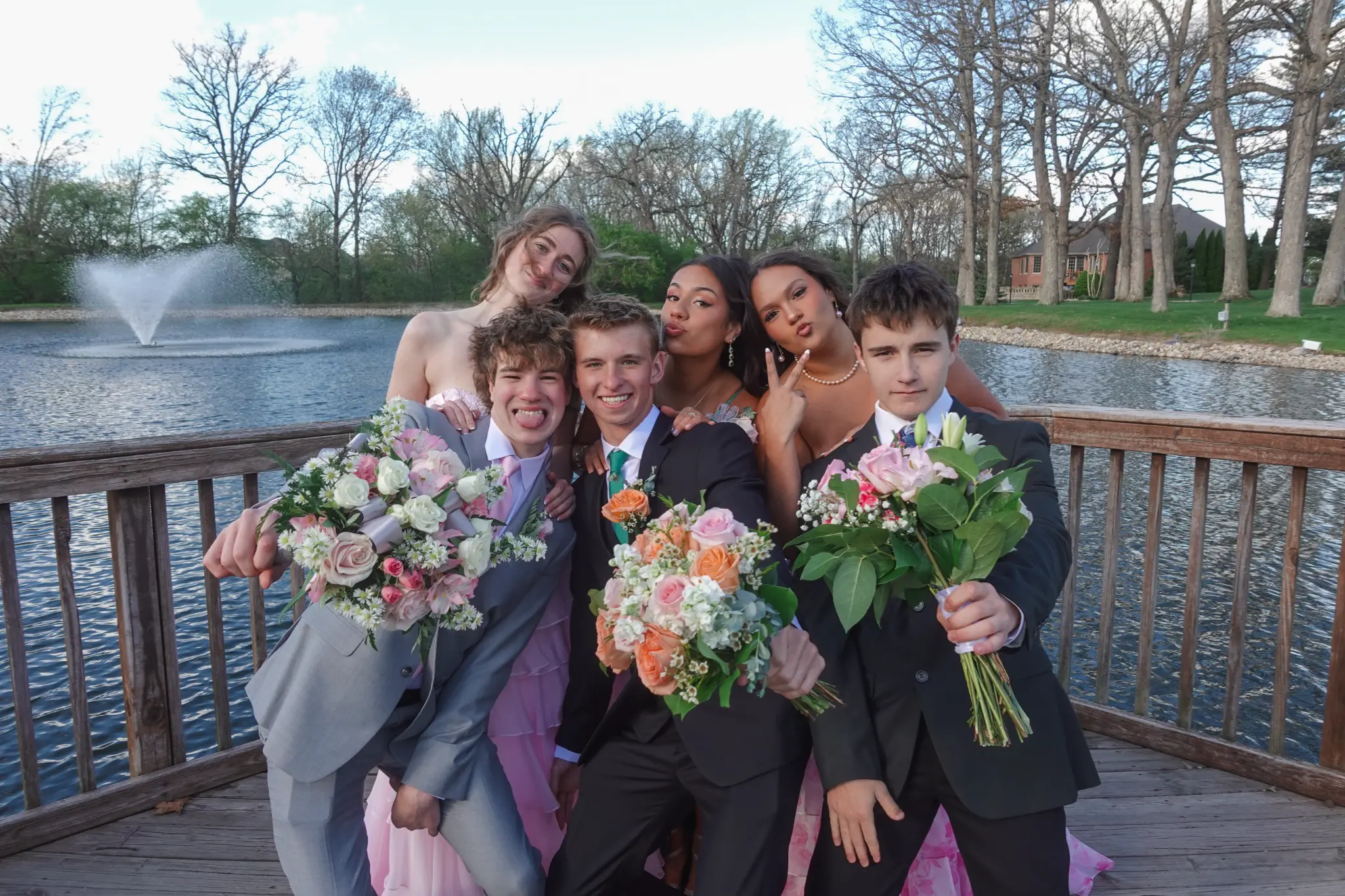 Prom group photo of friends posing on a wooden deck by the lake with bouquets in Northwest Indiana.