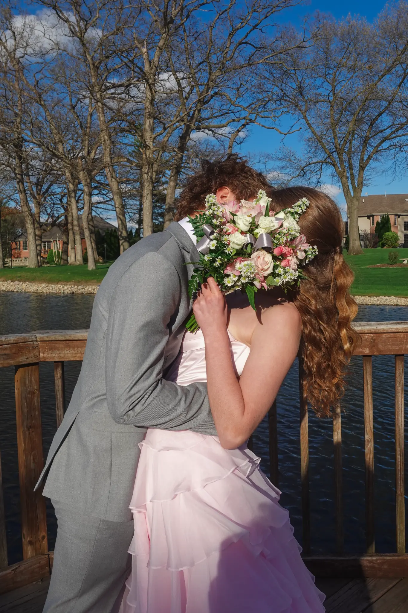 Prom couple kissing behind a bouquet on a bridge beside the water in Northwest Indiana.