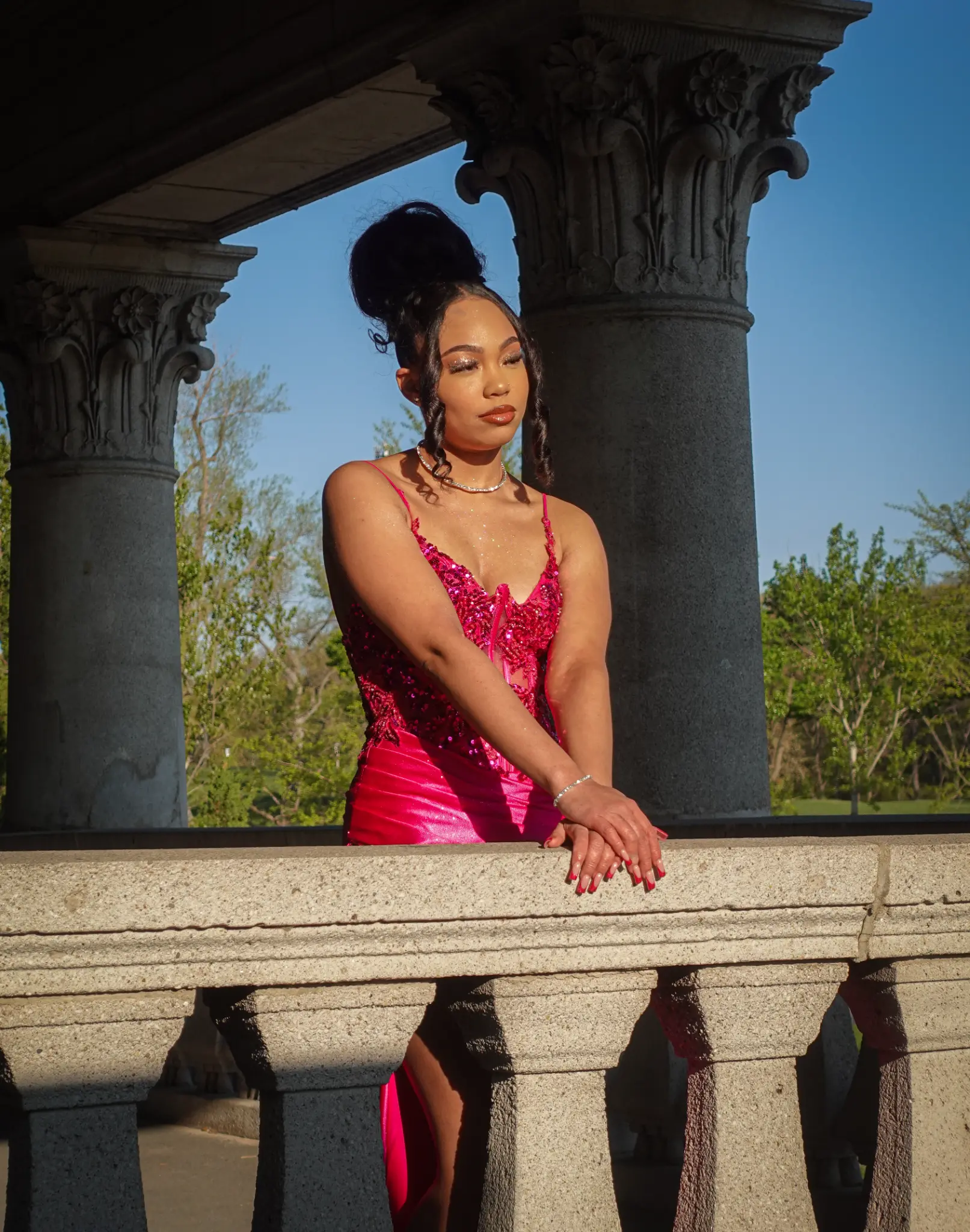 Prom portrait of a client in a bright pink dress standing on a stone balcony in Northwest Indiana.