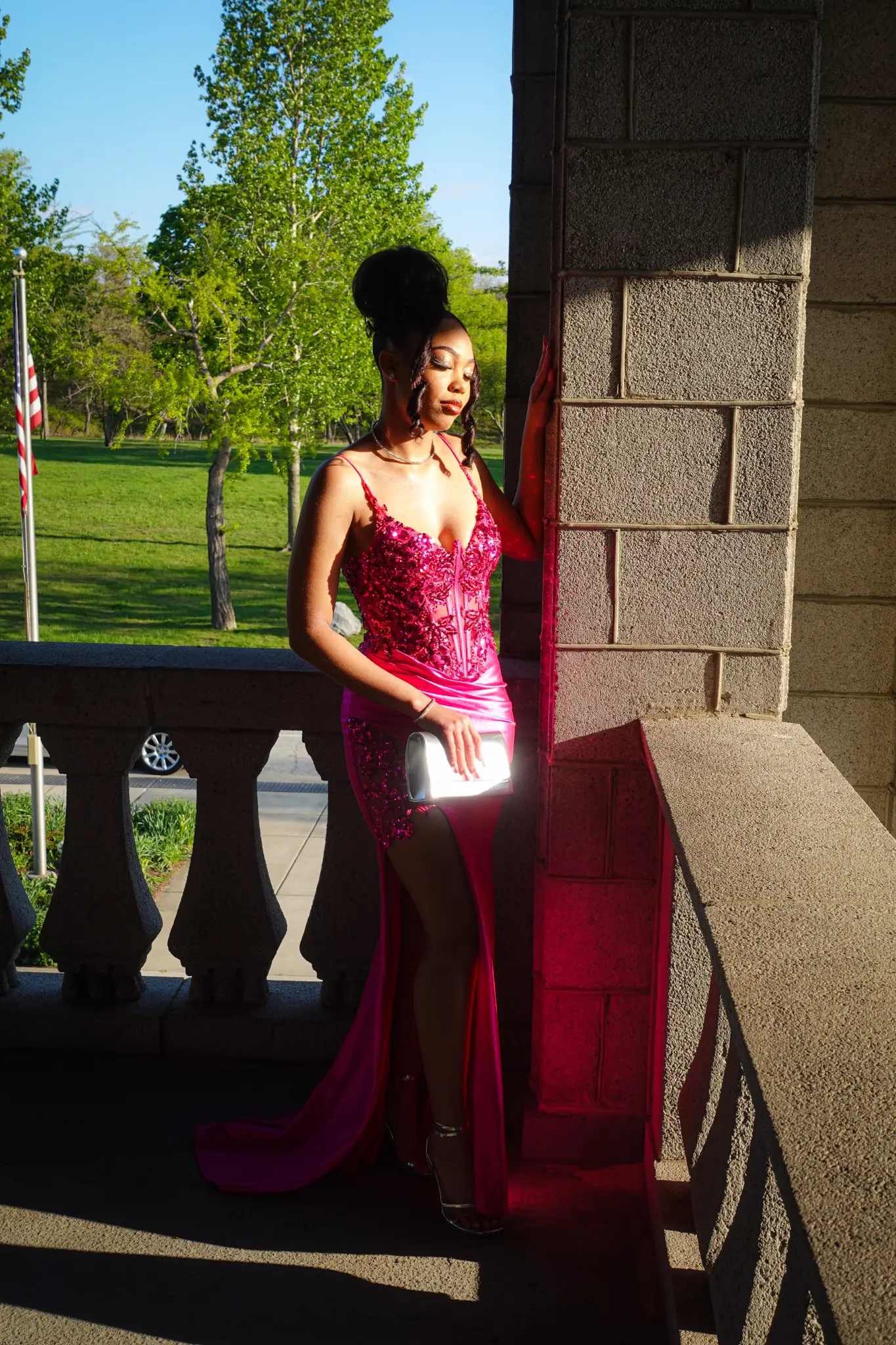Prom portrait of a client in a hot pink dress standing beside a sunlit stone column in Northwest Indiana.