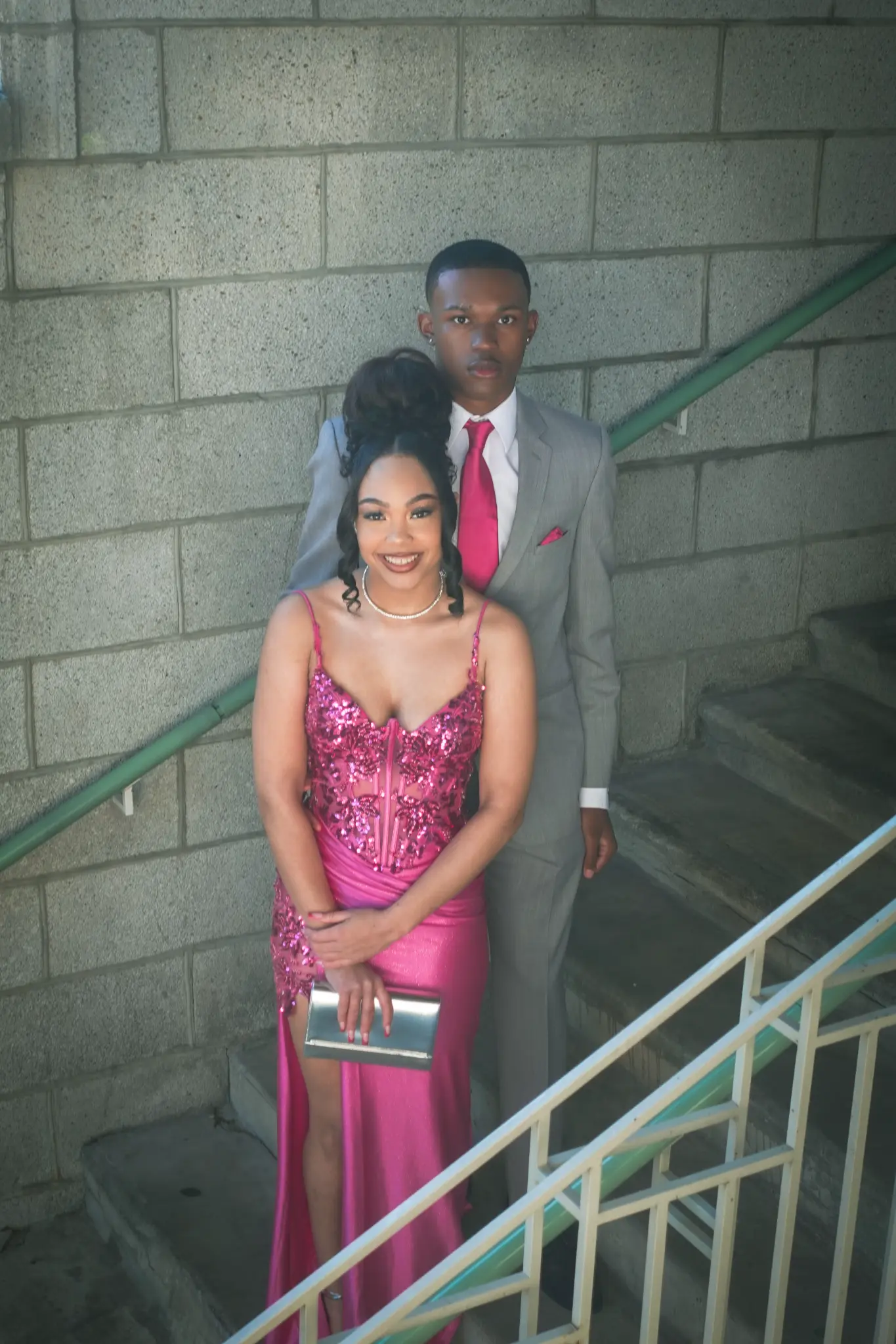 Prom couple portrait on a stairwell with the client in a bright pink dress and partner in a gray suit in Northwest Indiana.