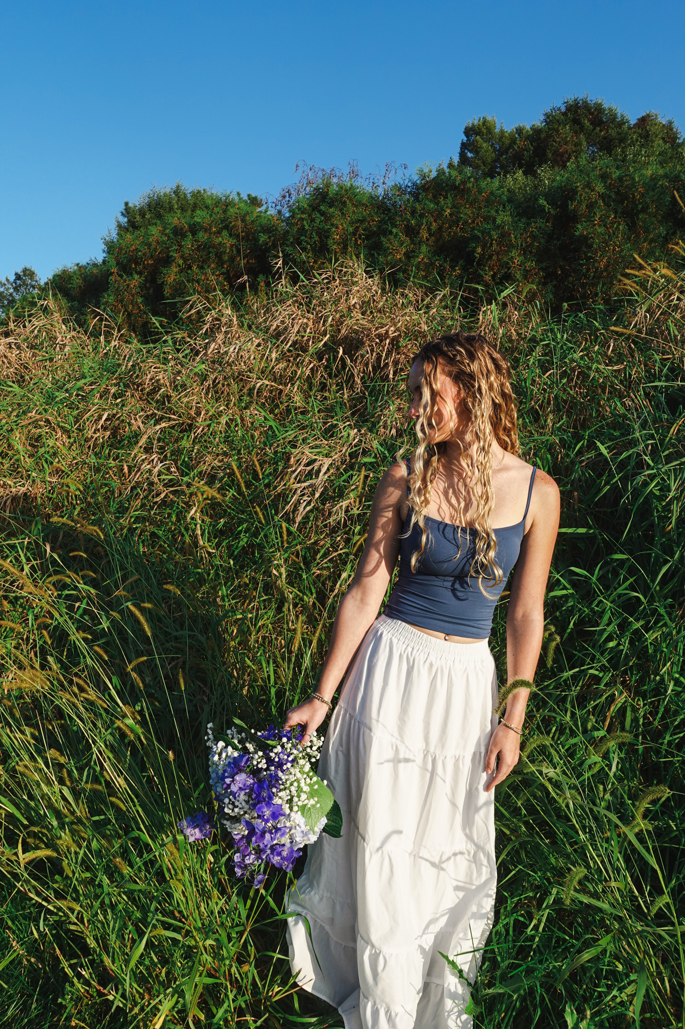 Senior portrait in tall grasses holding purple flowers photographed by Isabel Schilling Photography