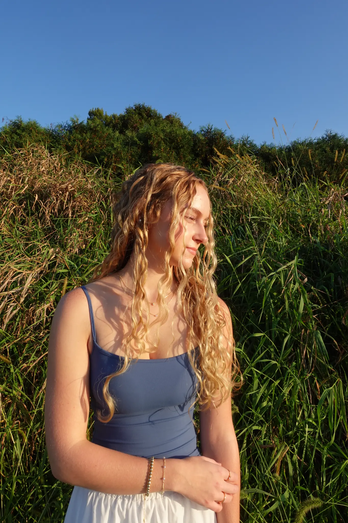 Outdoor senior portrait in warm sunlight with tall grasses and blue sky behind the client in Northwest Indiana.